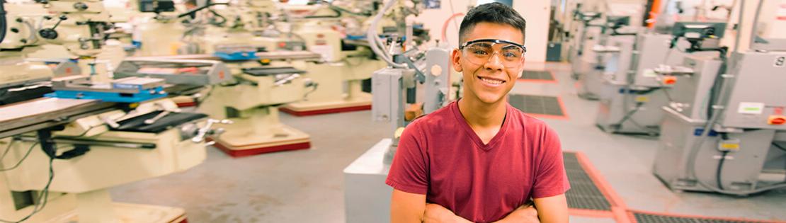 A student smiles in a warehouse with safety glasses on